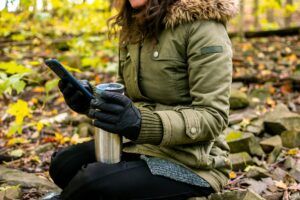 Woman in forest drinking coffee or tea in travel mug