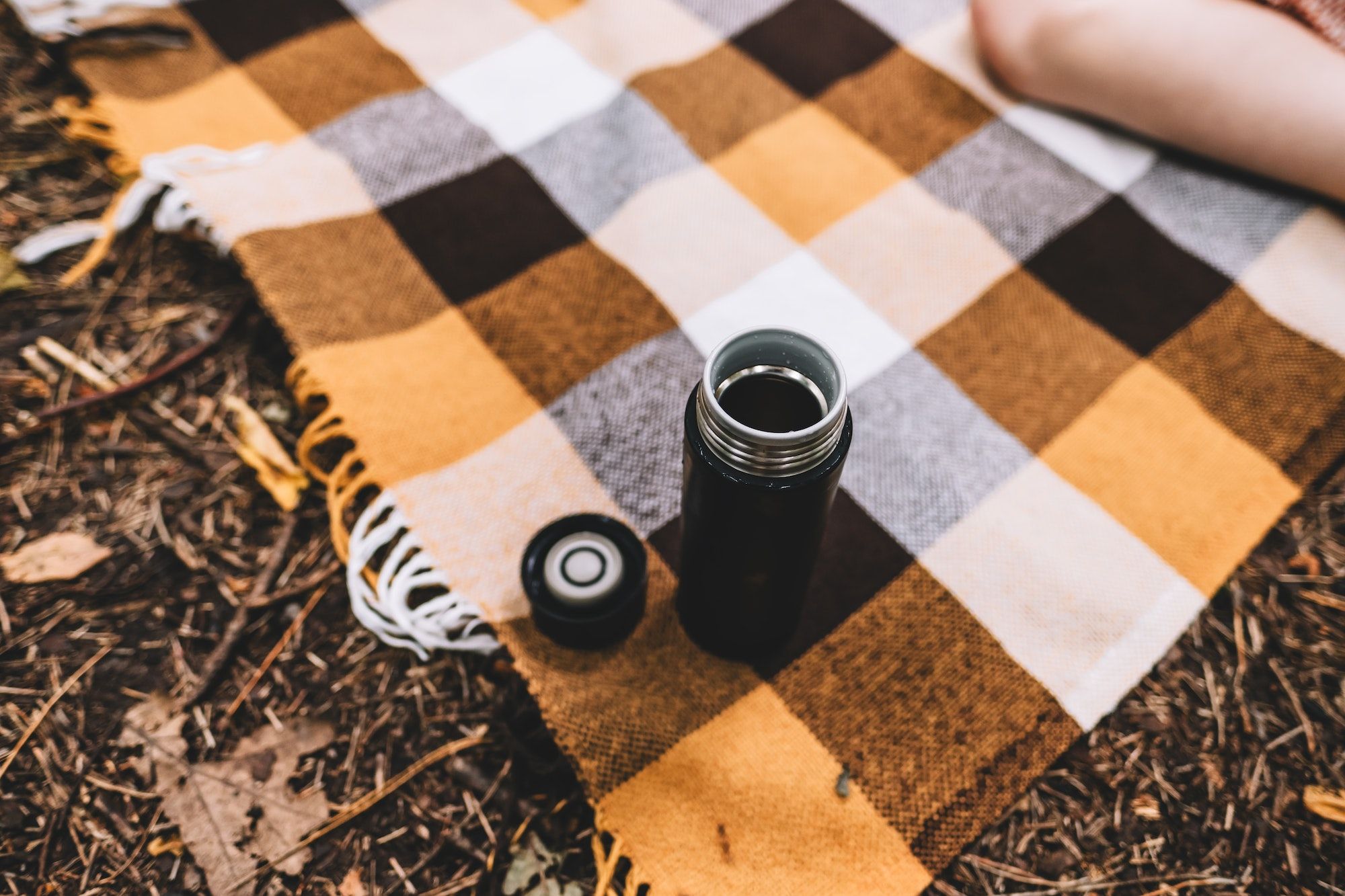 Black camping Thermos Coffee Mug on a plaid while hiking in the forest, outdoor recreation concept.